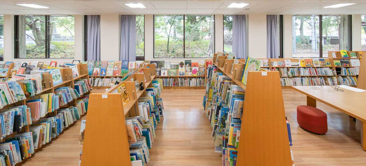 写真:図書館の中の様子。こどもが手に取りやすい高さの本棚が並んでいます。窓際の本棚にはたくさんの本の表紙が並んでいて、窓の向こうには緑が広がっています。