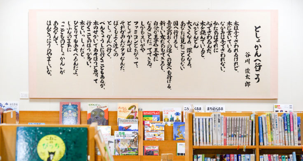 写真:谷川俊太郎さんの「としょかんへ行こう」の詩が本棚の上の壁に飾ってあります。