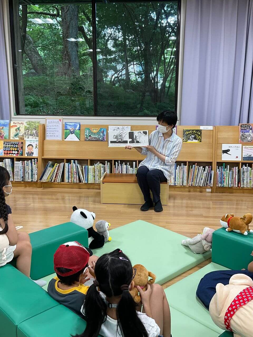 写真：図書館でこどもとぬいぐるみが読み聞かせを聞いています。