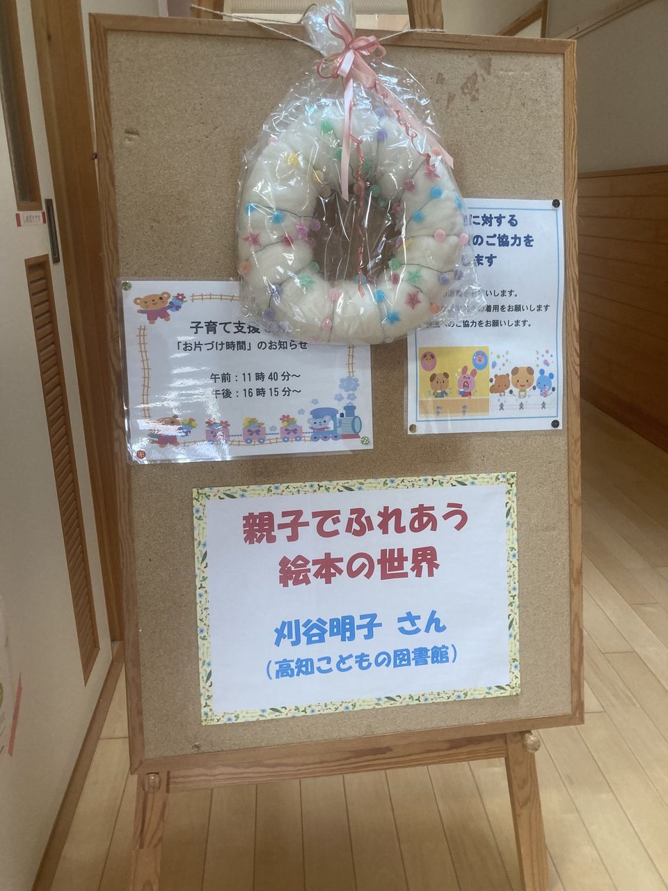 写真：手作りのリースと「親子でふれあう絵本の世界」の案内板です。