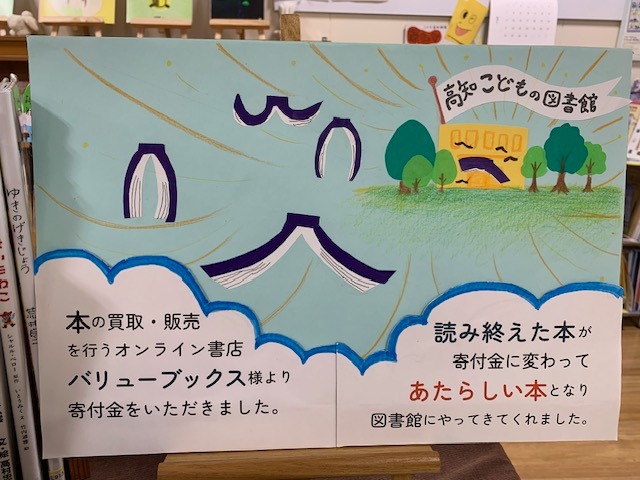 写真：バリューブックスの説明が書かれた案内板です。テキスト：本の買取、販売を行うオンライン書店バリューブックス様より寄付金をいただきました。読み終えた本が寄付金に変わってあたらしい本となり図書館にやってきてくれました。