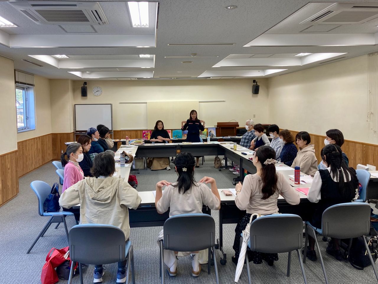 写真：参加者と講師が肩に手を置いて声を出すための体操をしています。