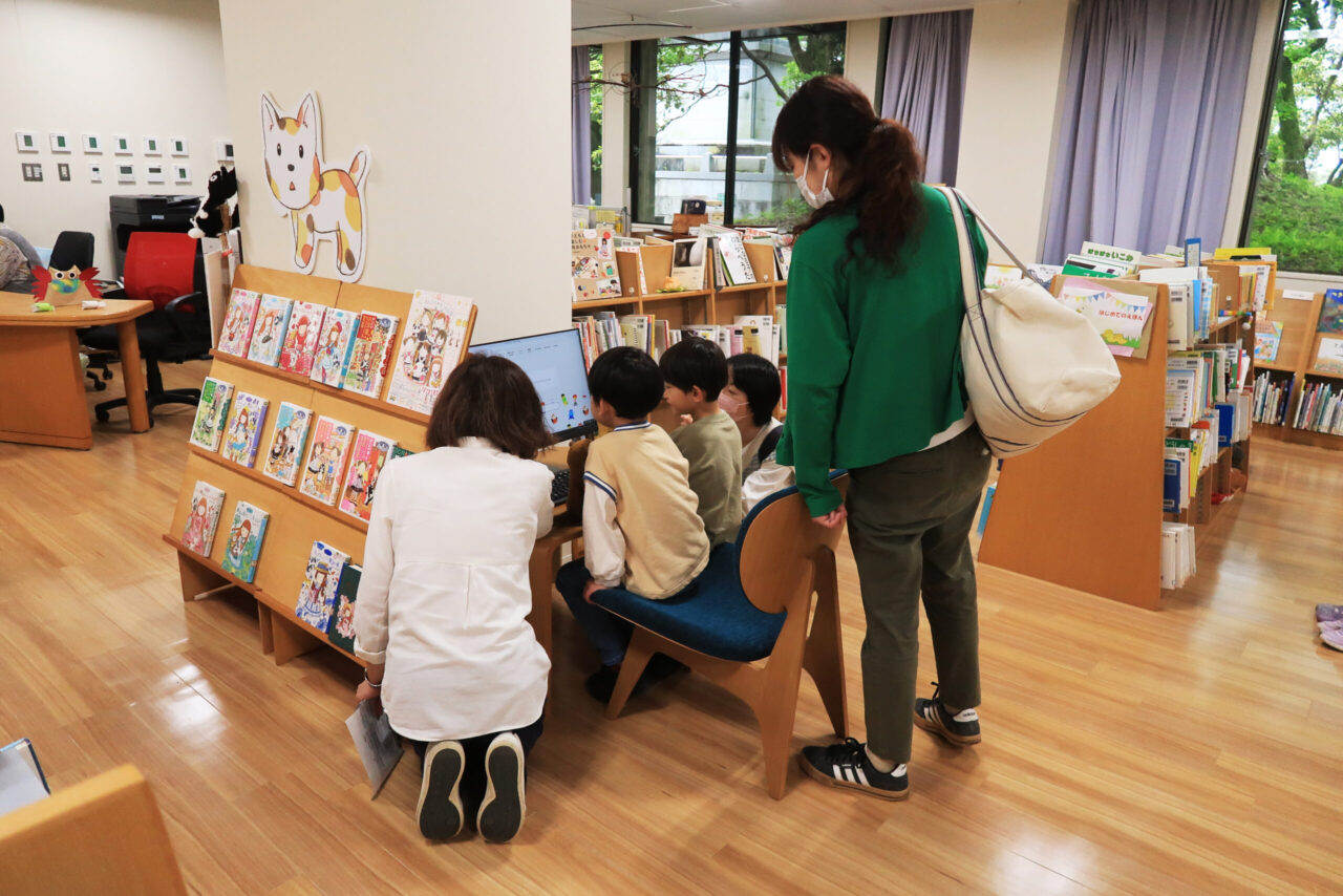写真：図書館のパソコンを見るこどもと大人たちです
