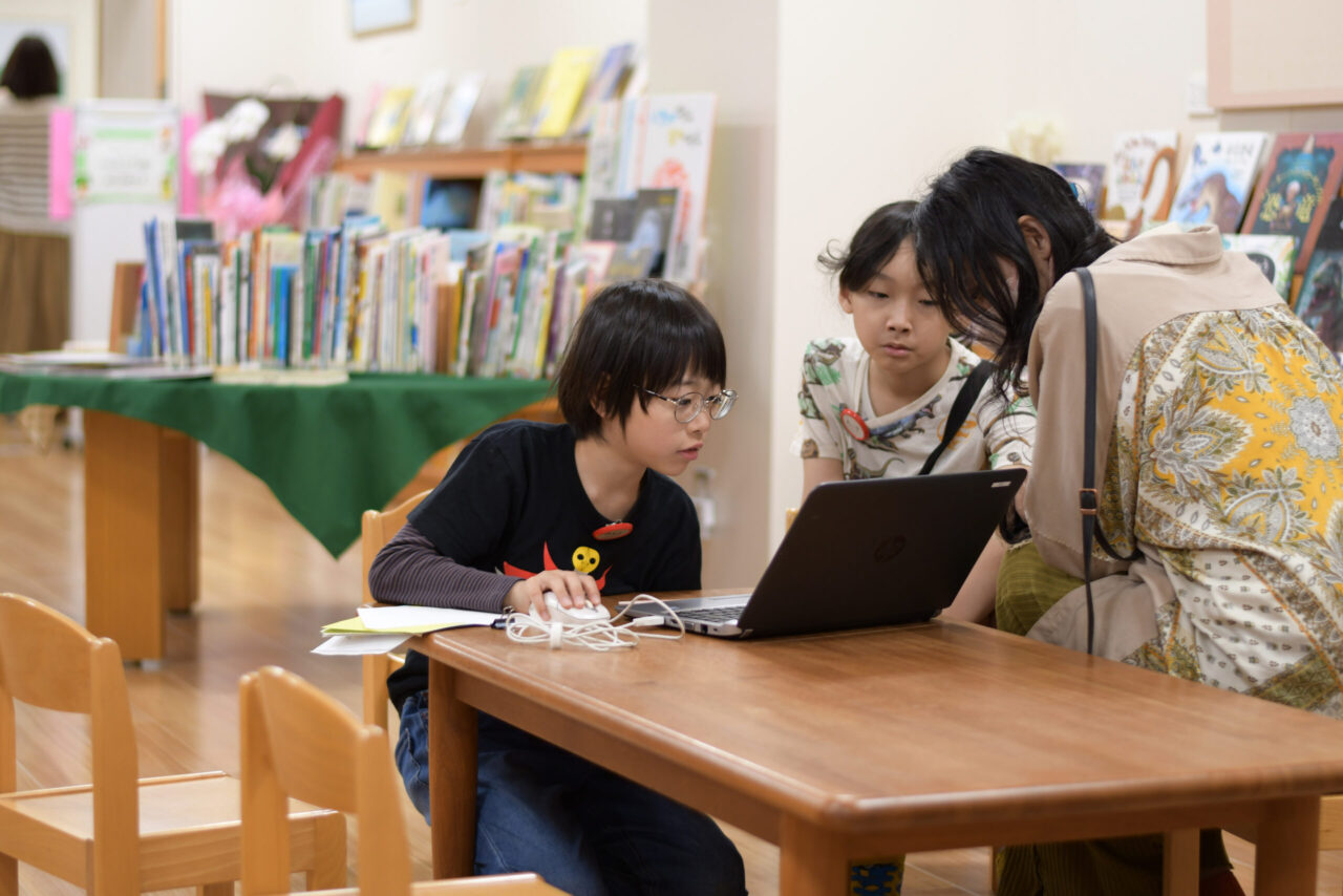 写真：ノートパソコンで調べているこども２人と見守る大人