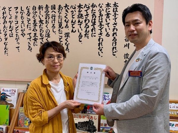 写真：大和証券上田喬史支店長様から田島館長が贈呈書を受け取っています。