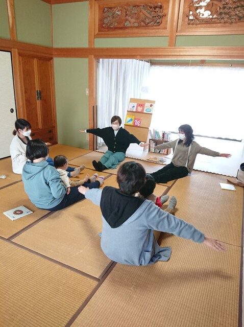 写真：赤ちゃんを抱っこして、畳の上に座って両手を広げています。