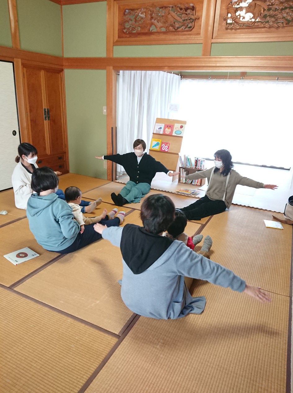 写真：赤ちゃんを抱っこして、畳の上に座って両手を広げています。